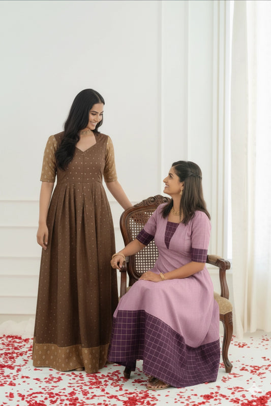 Two women in traditional outfits standing and sitting on a chair against a white curtain background.