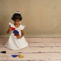 a little girl in a white dress holding a teddy bear 